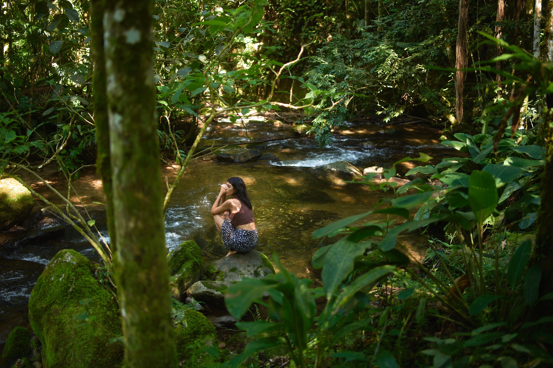 Mulher sentada perto de um rio cercado por mata.